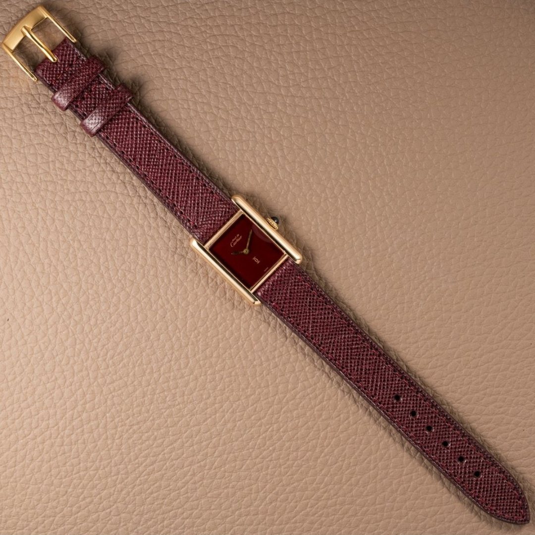 The whole watch laid out flat with the burgundy lizard strap and its gold buckle extended.