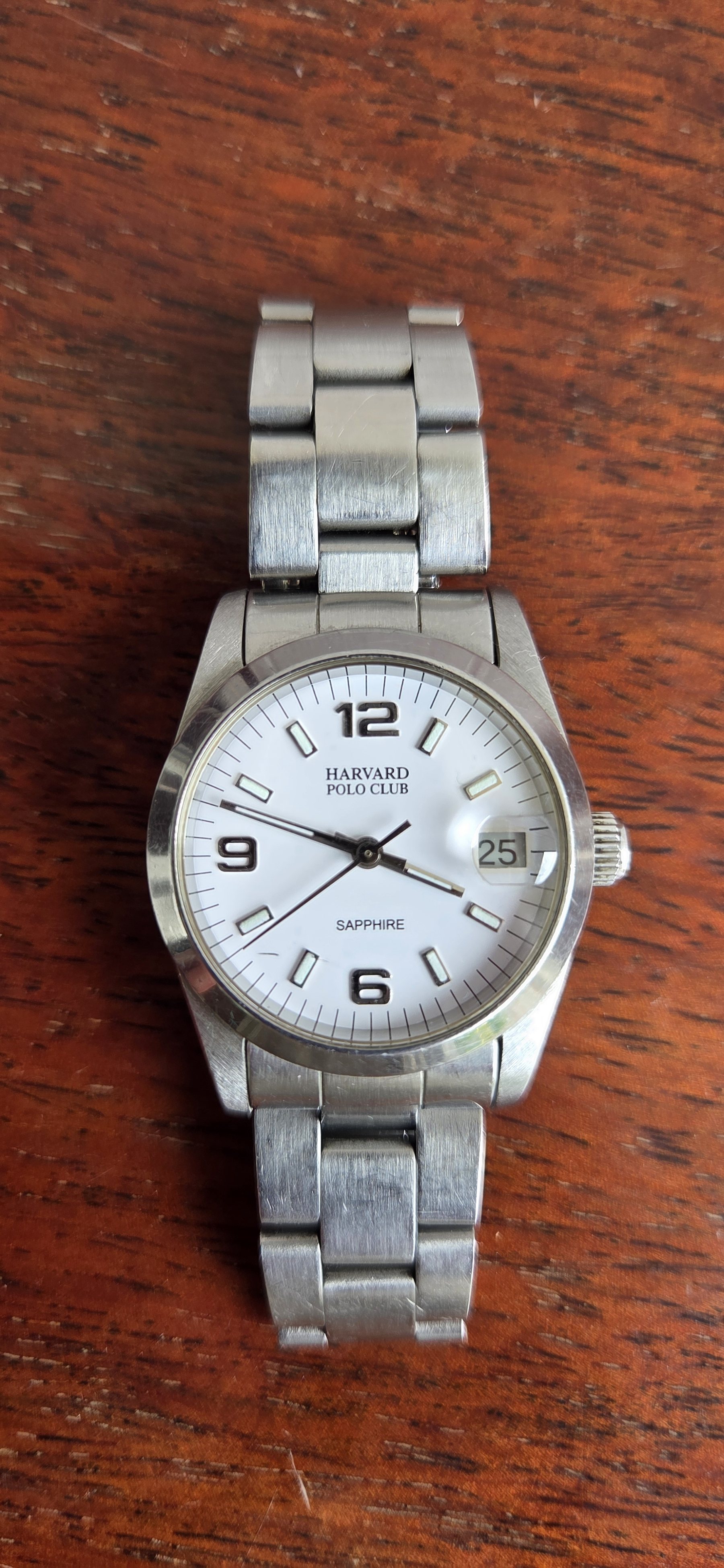 The watch at an angle, the bracelet curving away across a wooden table.