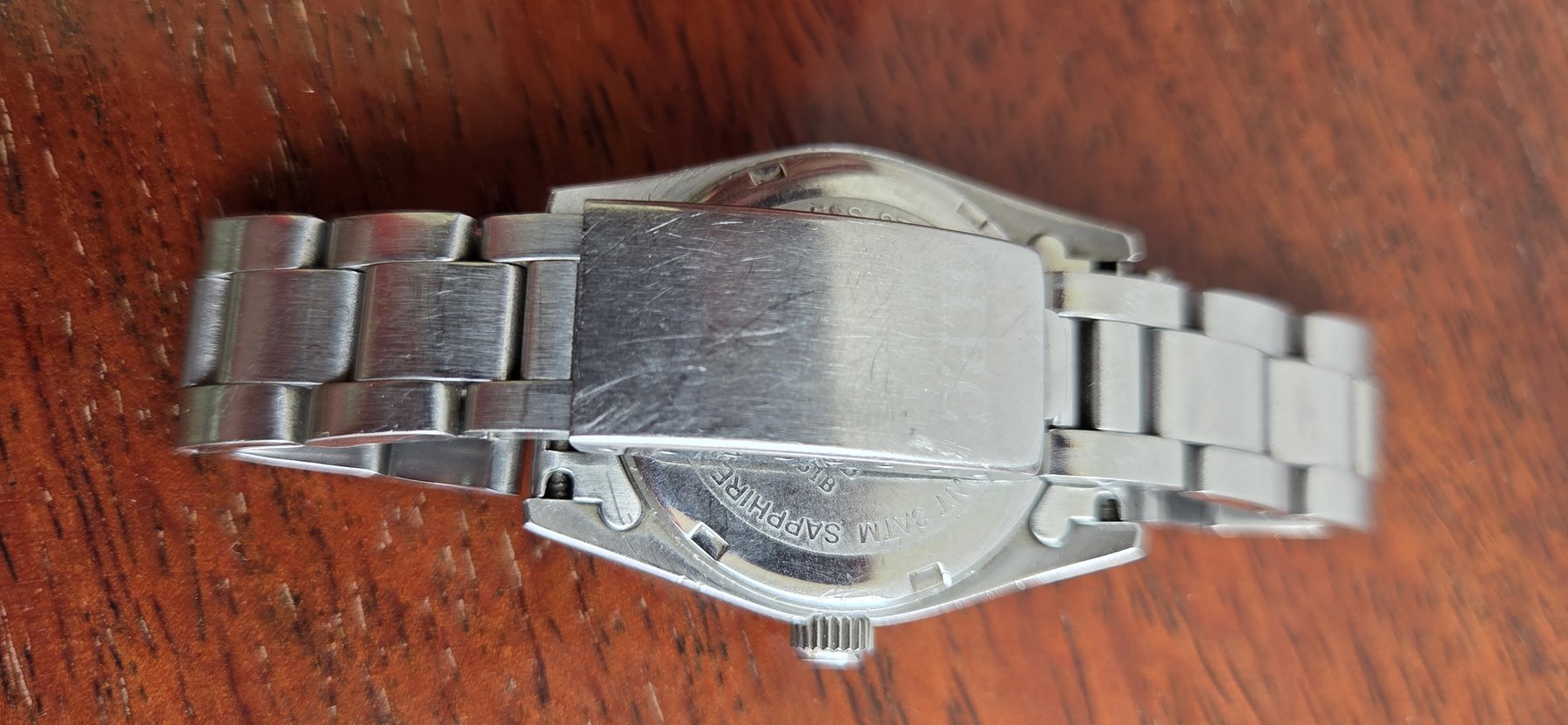 The folding clasp of the steel bracelet, open on the table.