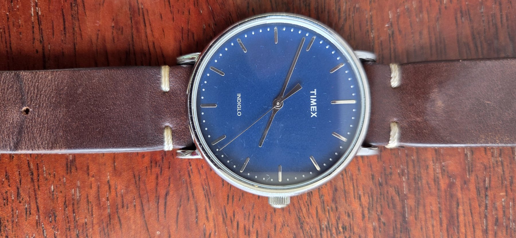 A Timex wristwatch with a deep blue dial and slim baton markers, on a brown leather strap.