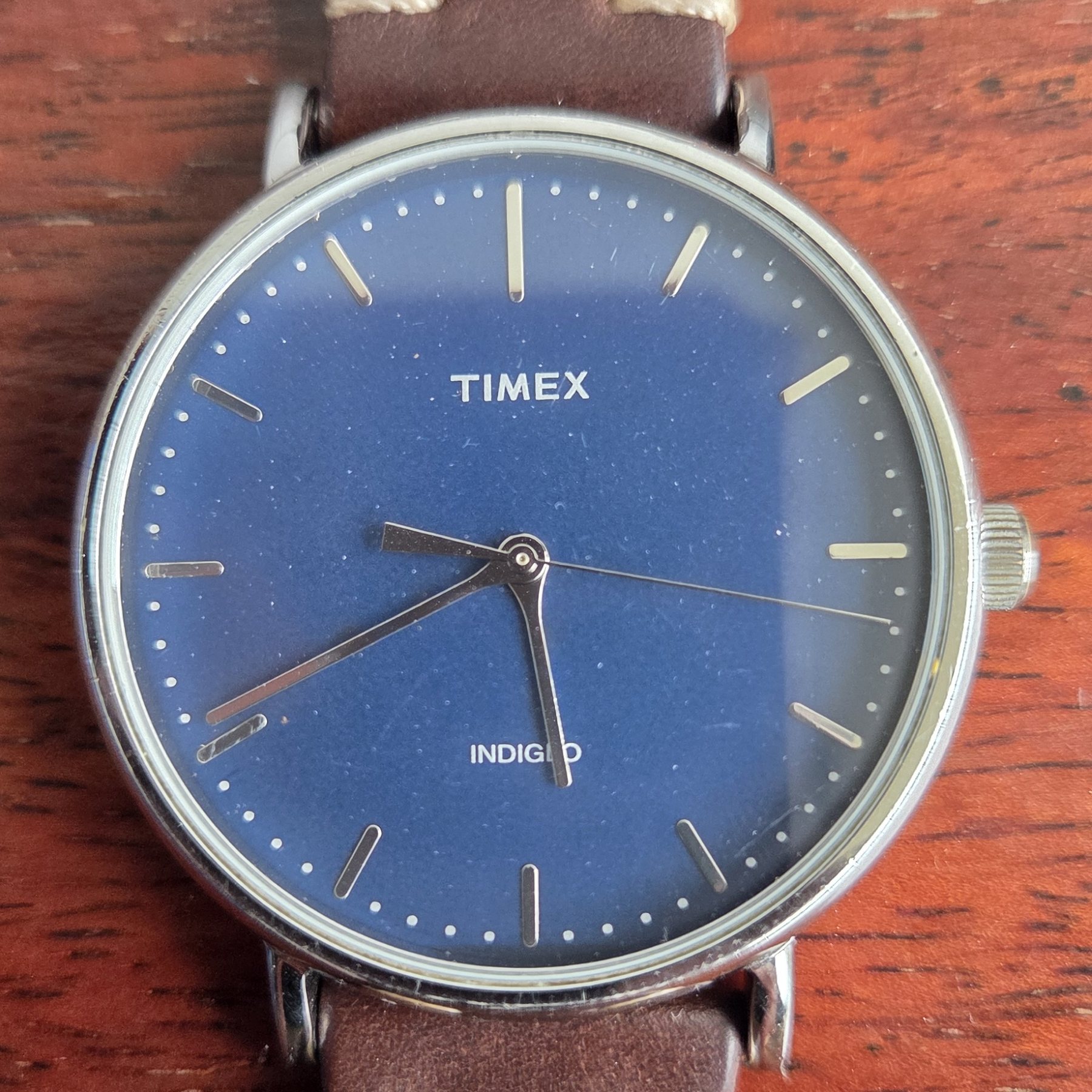 A Timex wristwatch with a deep blue dial and slim baton markers, on a brown leather strap.