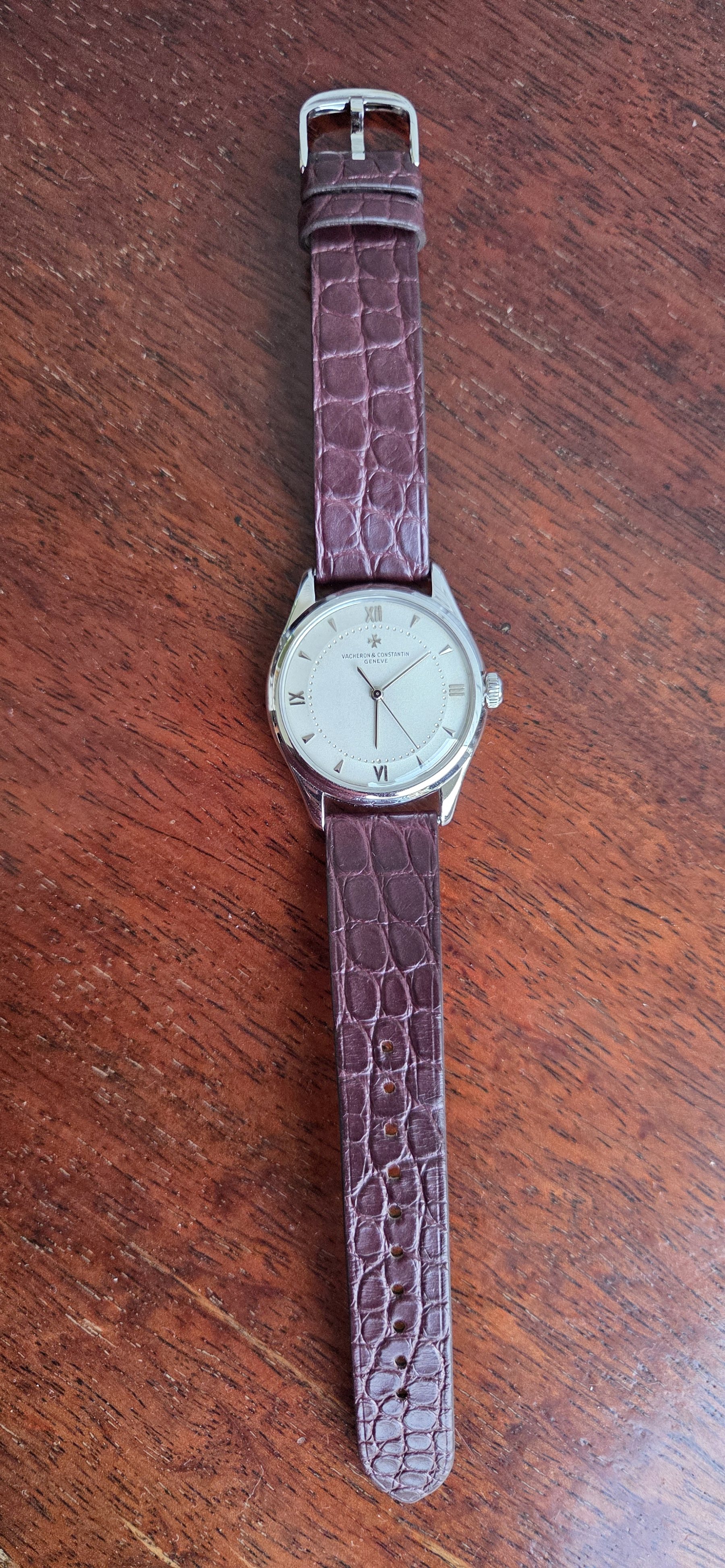 The whole watch laid out flat on a wooden table with its burgundy alligator strap extended.