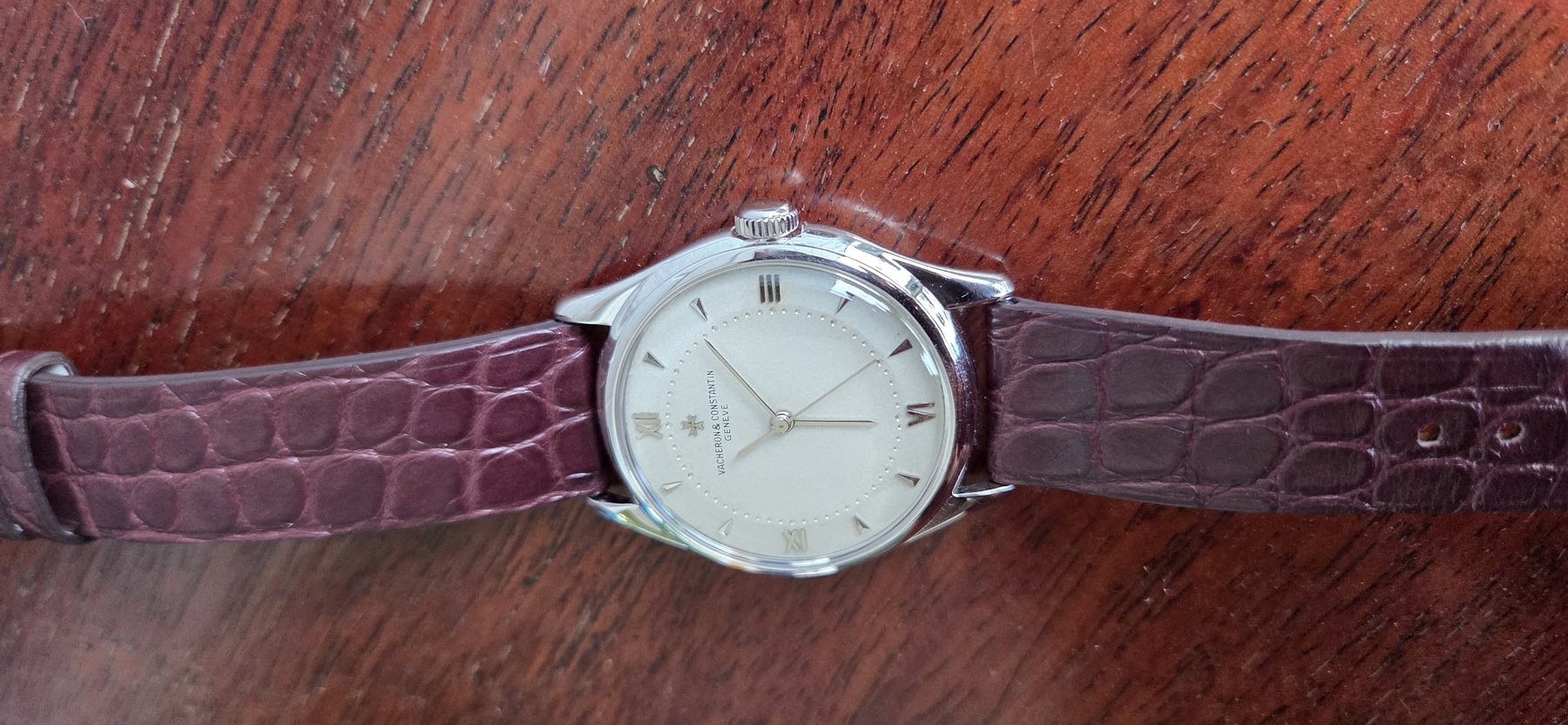 The watch at a low three-quarter angle, light raking across the silvered dial.