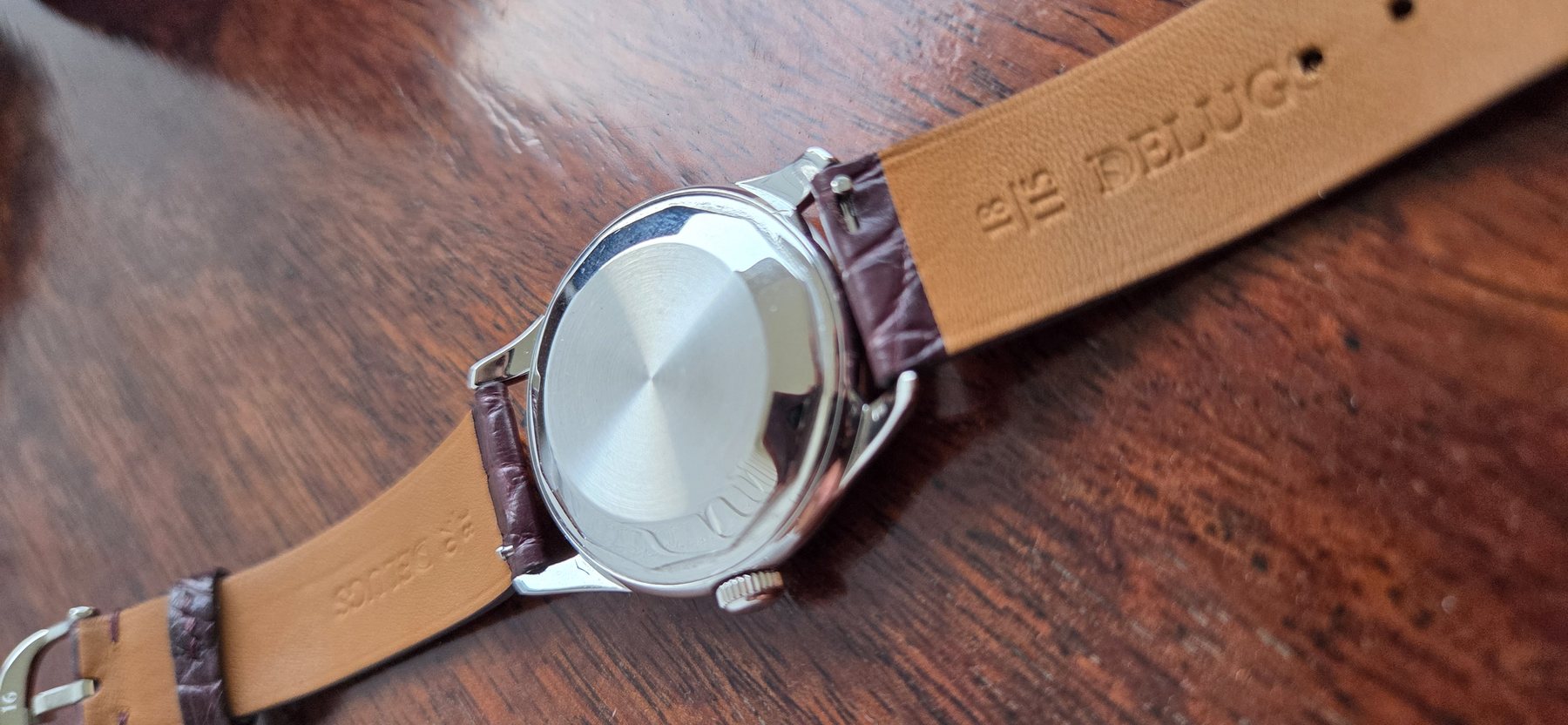 The case back at an angle, with the tan underside of the strap stamped 18mm Delugs.