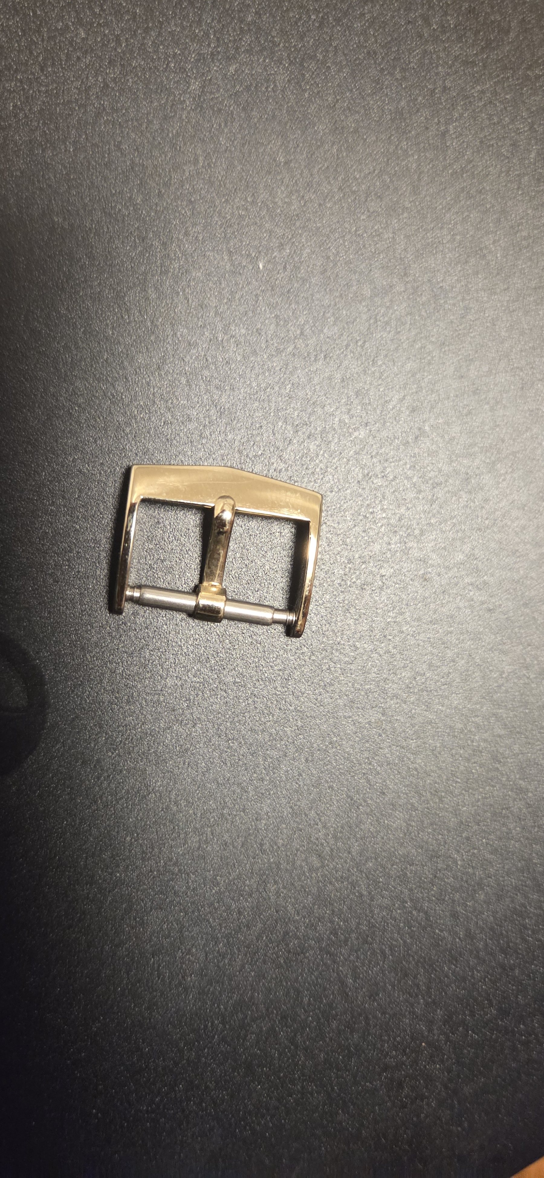 The signed gold buckle, photographed alone against a dark background.