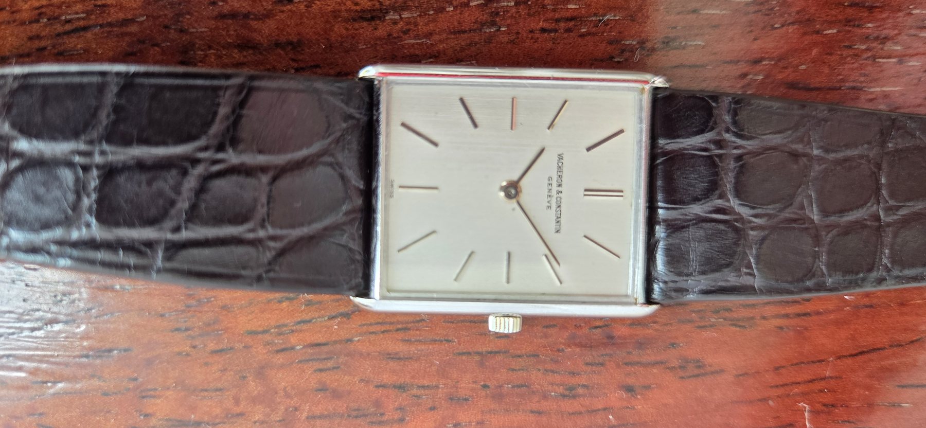 The watch on its black alligator strap, laid on a wooden table.