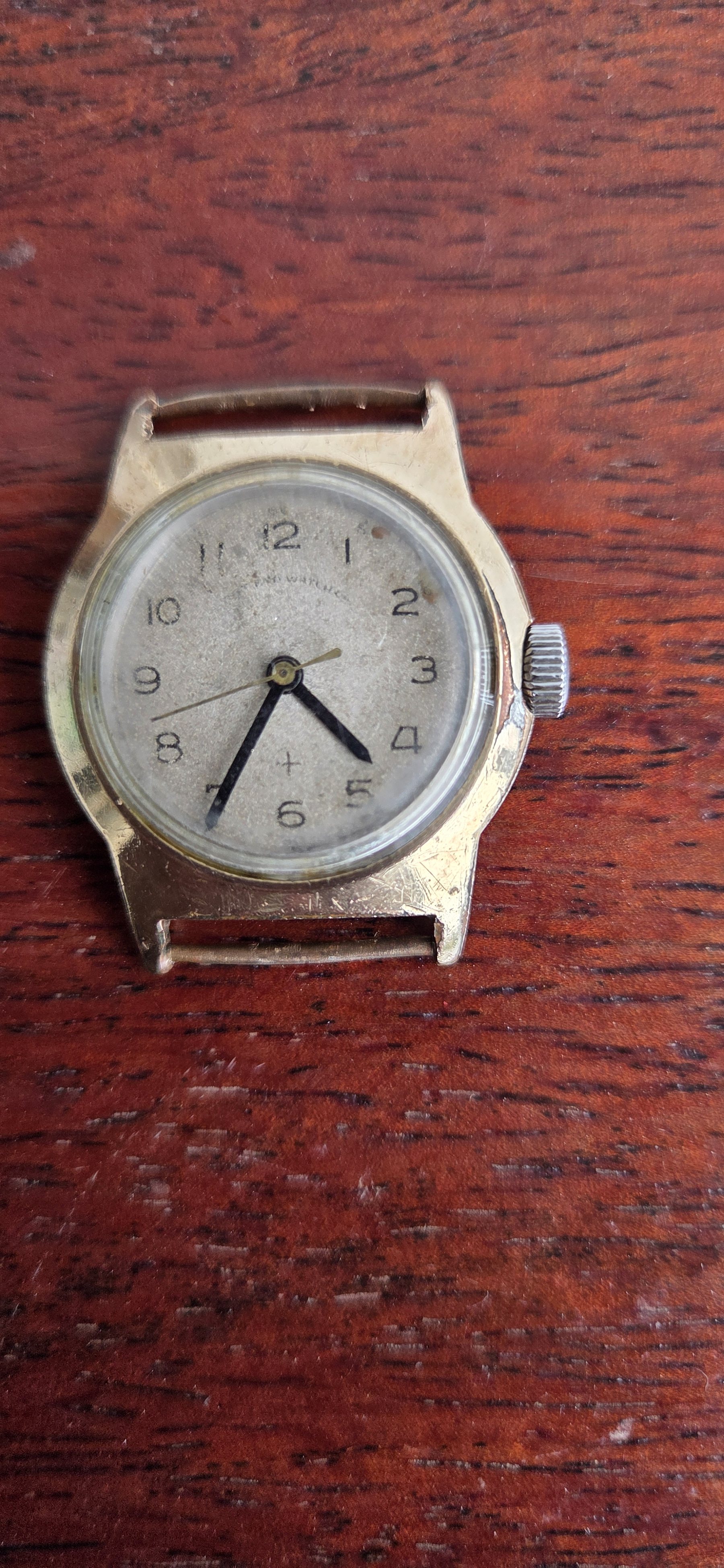 The watch with no strap fitted, laid face-up on a wooden table.